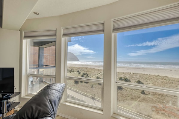 A room with large windows overlooking a beach, a television, and a leather couch.