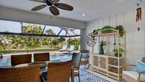 A poolside area with wicker furniture, a ceiling fan, a clock, and a plant shelf. - The Salty Peacock near Englewood Beach (Rotonda West)