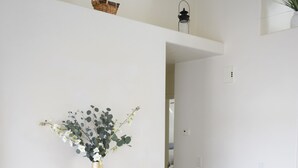 Ein Flur mit einer weißen Wand, einem hölzernen Regal mit Blumenvase und einem schwarzen Laternenleuchter an der Wand.