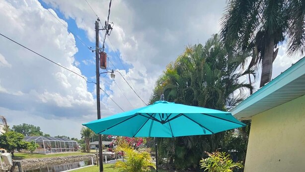 A patio with a wicker sofa set, a table, and a large umbrella. - Pet friendly, waterfront property on a canal off of the Caloosahatchee River (Fort Myers)