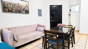 A living room with a sofa, a dining table with chairs, a black door, and a painting on the wall. - CABO DOWNTOWN STUDIOS: 1BR Studio 2 doubles perfect location close to marina #3 (Cabo San Lucas)