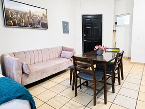 A living room with a sofa, a dining table with chairs, a black door, and a painting on the wall. - CABO DOWNTOWN STUDIOS: 1BR Studio 2 doubles perfect location close to marina #3 (Cabo San Lucas)