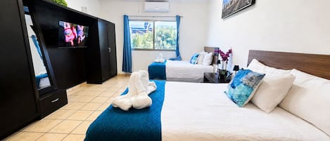 A hotel room with a bed, a TV, a ceiling fan, a window with curtains, and a painting on the wall.