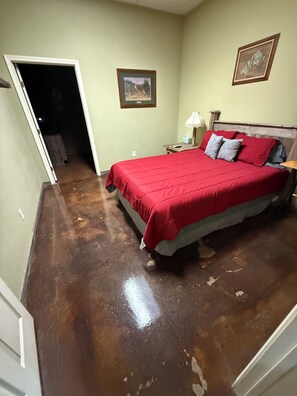 A bedroom with a large bed, a nightstand, a lamp, and a door leading to another room.