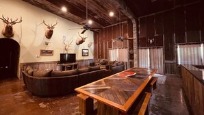 Un intérieur rustique avec un plafond en bois, des têtes d’animaux empaillées accrochées aux murs, une grande table à manger en bois et un coin salon confortable.