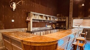 Un espace bar avec des tabourets en bois, un comptoir et une étagère où sont disposés des verres et une horloge.