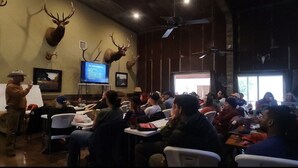 Une pièce dont les murs sont ornés de têtes de cerf empaillées, avec un téléviseur et des personnes assises à des tables.