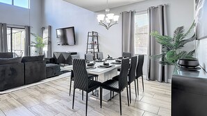 Ein moderner Essbereich mit Tisch, Stühlen, einem Fernseher und einer Chandelier.