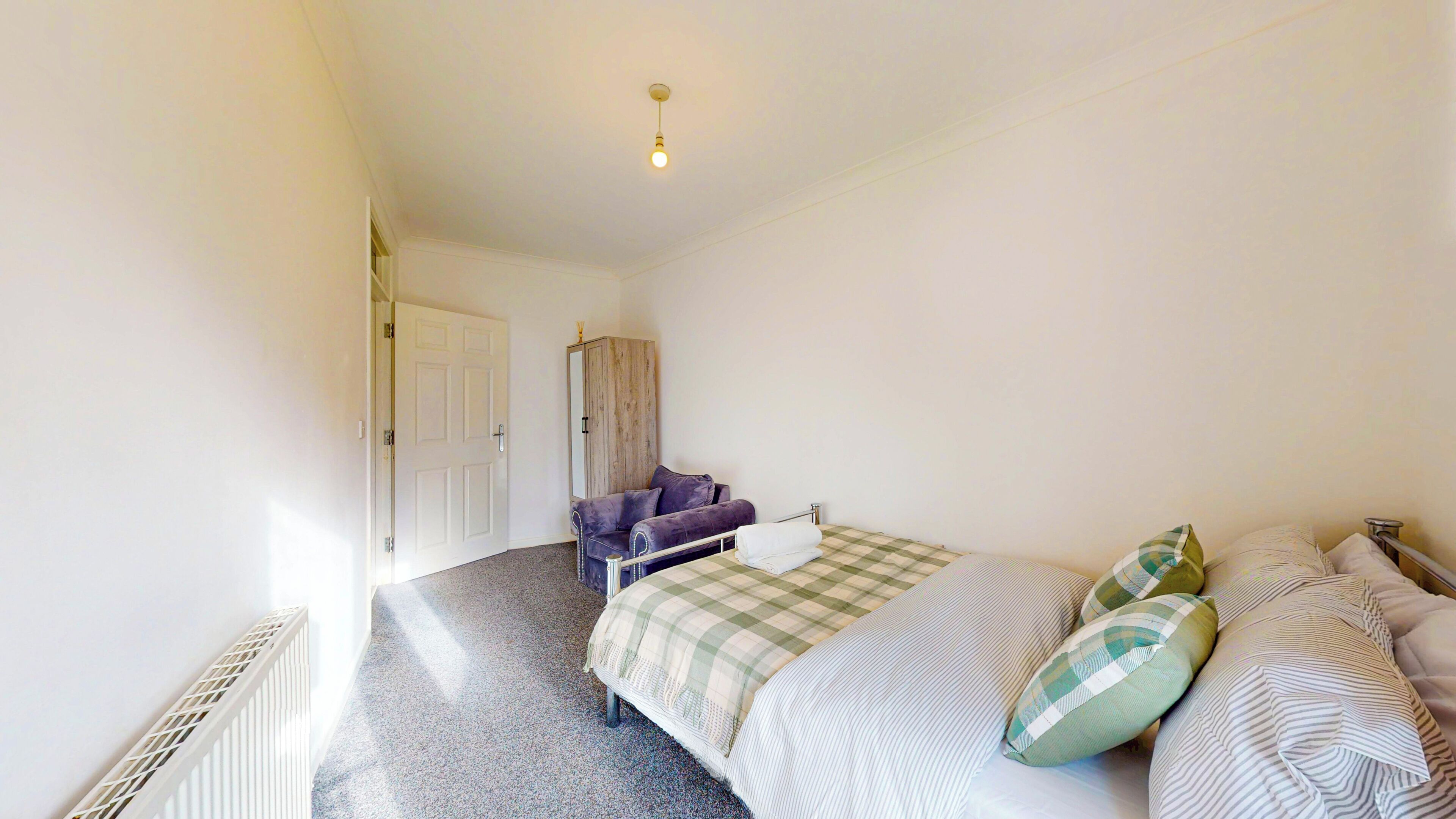 A bedroom with a bed, a chair, a wardrobe, and a radiator.