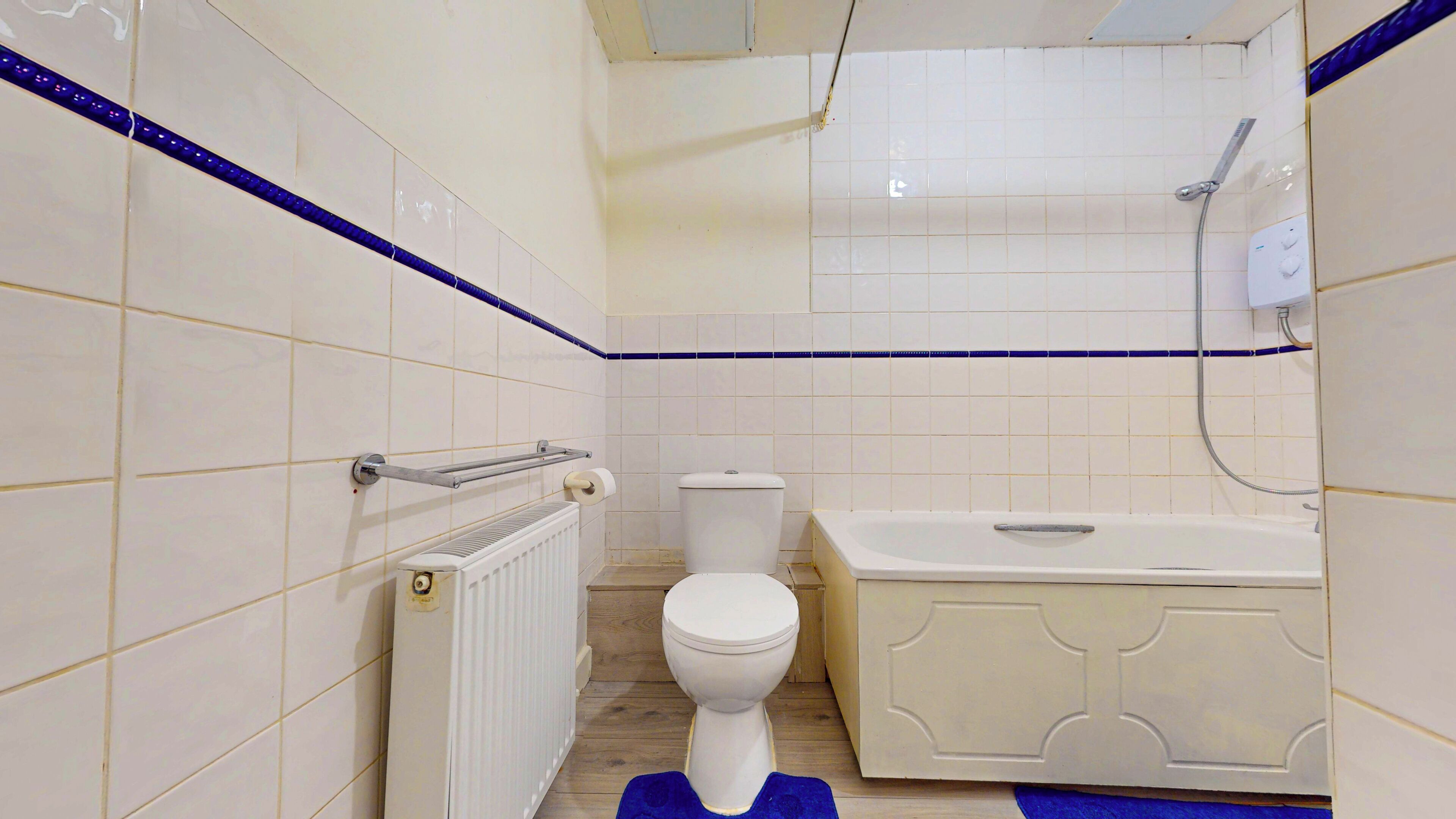 A bathroom with white tiles, a toilet, a bathtub, and a shower.