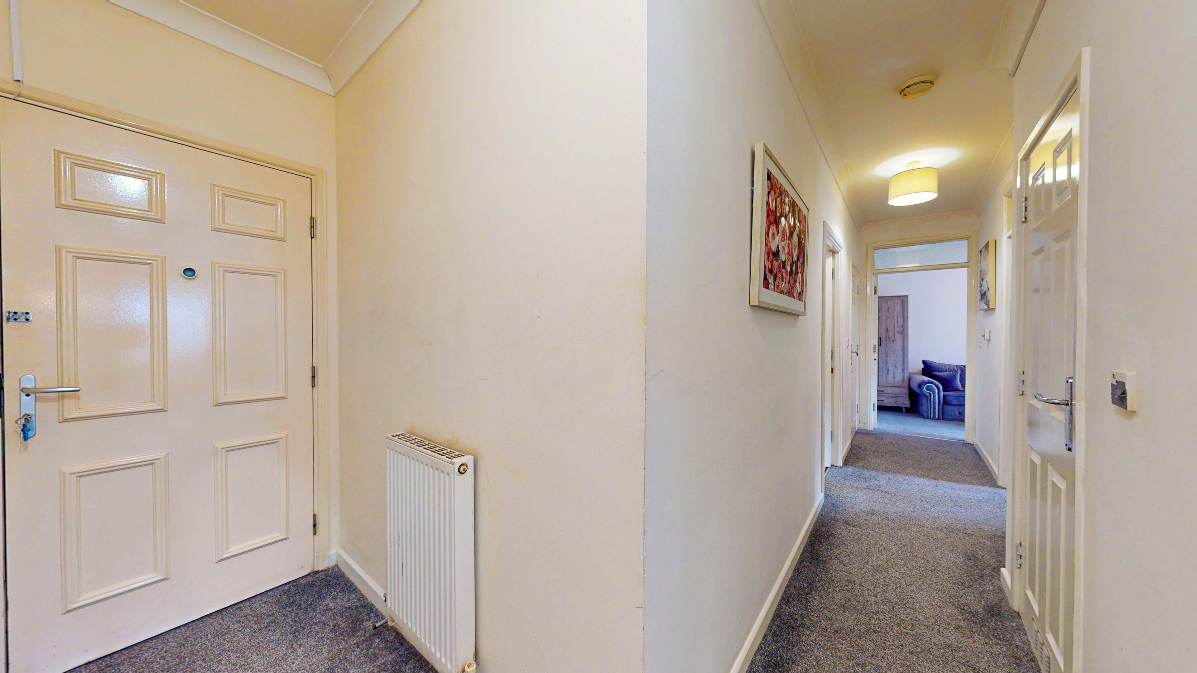 Un couloir avec des portes blanches, un radiateur et un tableau encadré accroché au mur.