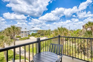 A balcony with a table and chairs, overlooking a street with houses and palm trees. - 🌊Island Palm | Ocean and River Views | Walk to No Drive Beach 🌊 (New Smyrna Beach)