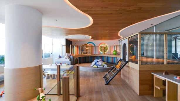 Un intérieur moderne avec un plancher en bois, un espace de jeux doté d’équipements colorés et un coin salon offrant une vue agréable.