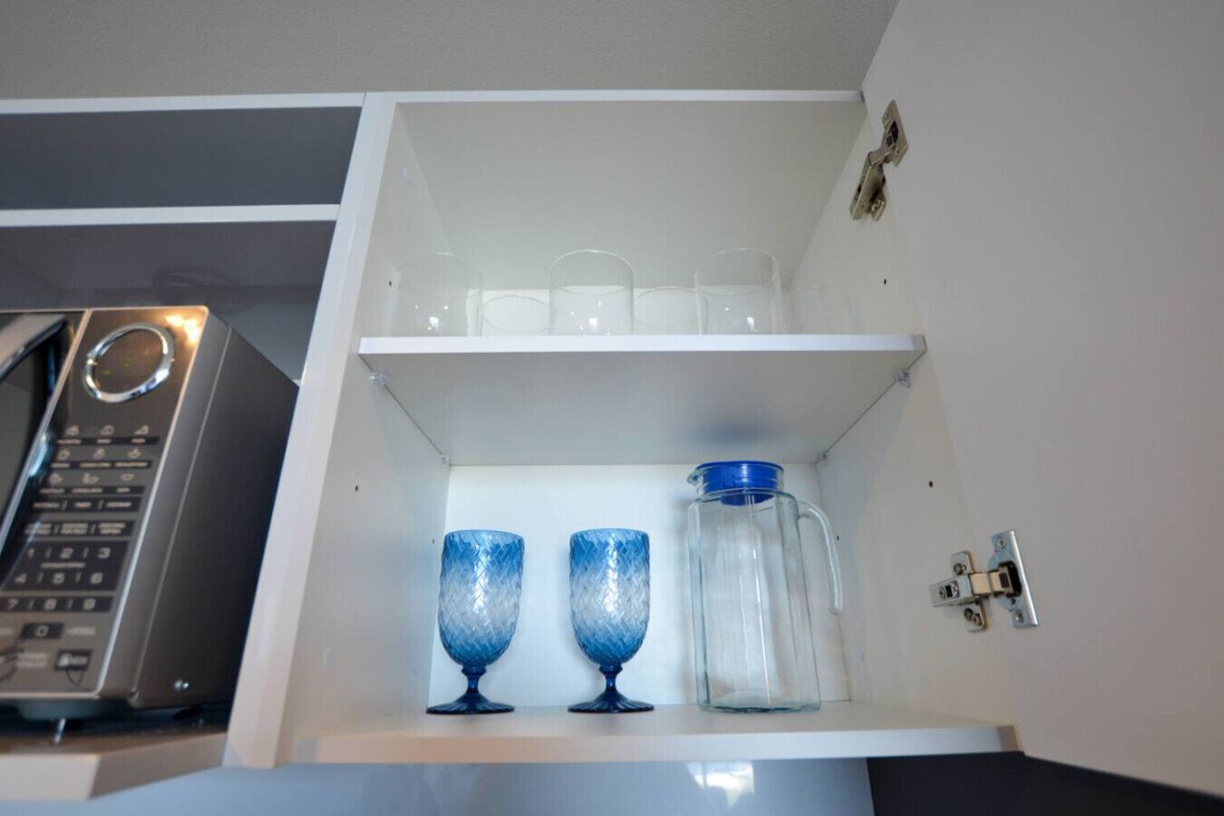 Cozinha com micro-ondas, um armário com dois copos de vidro azul e um jarro de vidro transparente.
