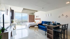 Un appartement moderne comprenant un lit, un canapé bleu, un coin repas et une grande fenêtre donnant sur la ville.