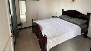 A bedroom with a bed, a television mounted on the wall, a mirror, and a door.