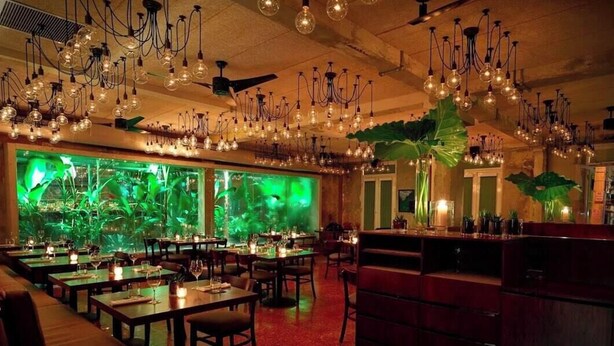Ein Restaurant mit mehreren Speisetischen, hängenden Lampen und einem großen Aquarium.