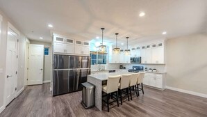 Una cocina moderna con armarios blancos, electrodomésticos de acero inoxidable y una isla central con taburetes de bar.