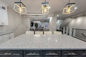 A modern kitchen with a large island, pendant lights, and a staircase.