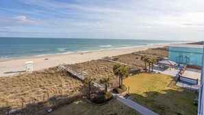Vue sur la plage depuis un bâtiment doté d’un patio, d’une tour de surveillance et d’une promenade qui mène à la plage.