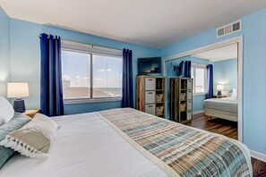 Un dormitorio con cama, cómoda, televisor y ventana con cortinas.