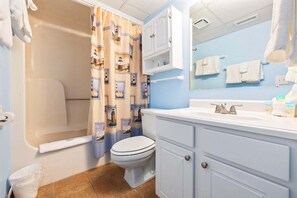 A bathroom with a bathtub, toilet, vanity with a mirror, and a shower curtain with a lighthouse pattern.