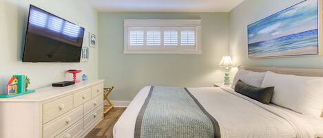 A bedroom with a bed, a television, a window, and a painting on the wall.