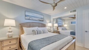 A bedroom with a bed, nightstands, lamps, a ceiling fan, a painting, and a mirror. - Oceanfront retreat in Carolina Beach 0910 (Carolina Beach)