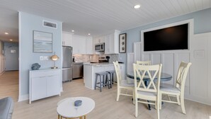 A modern kitchen with white cabinetry, a central island, and a dining area with striped chairs. - Oceanfront retreat in Carolina Beach 0910 (Carolina Beach)