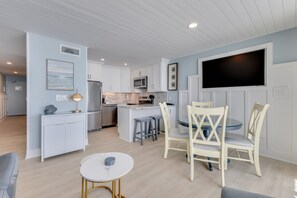 Une cuisine moderne avec des meubles blancs, un îlot central et un coin repas doté de chaises à rayures.