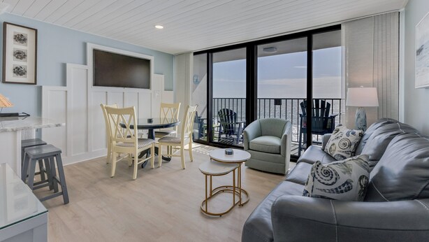 A modern living room with a sofa, chairs, a small table, and a balcony with outdoor seating. - Oceanfront retreat in Carolina Beach 0910 (Carolina Beach)