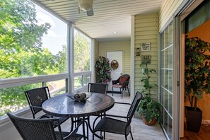 Een overdekt terras met een ronde tafel en stoelen, een deur met een krans, en potplanten.