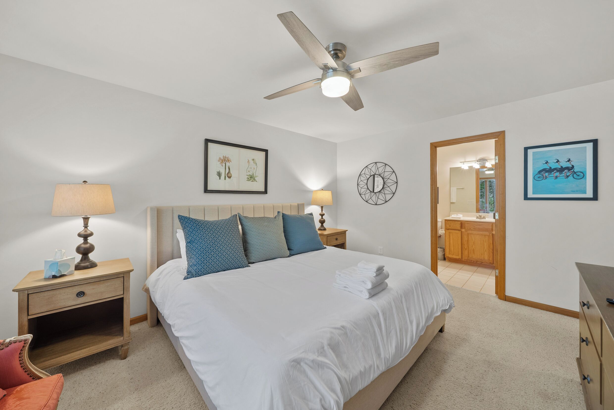 A bedroom with a bed, nightstands, a ceiling fan, a wall-mounted mirror, and a door leading to a bathroom.