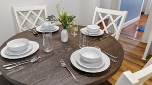 A round dining table with white plates, bowls, and cutlery, accompanied by a vase with flowers and clear glassware. - Elegant Harvard Free Parking • Prime Location, 2 Bed 1 Bath (Cambridge)