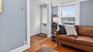 A room with a brown leather sofa, a lamp, and a window with blinds. - Elegant Harvard Free Parking • Prime Location, 2 Bed 1 Bath (Cambridge)