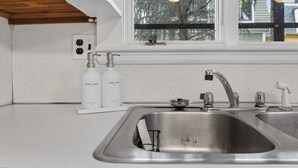 A kitchen with a stainless steel sink, a window with a view of trees, and a white countertop. - Elegant Harvard Free Parking • Prime Location, 2 Bed 1 Bath (Cambridge)
