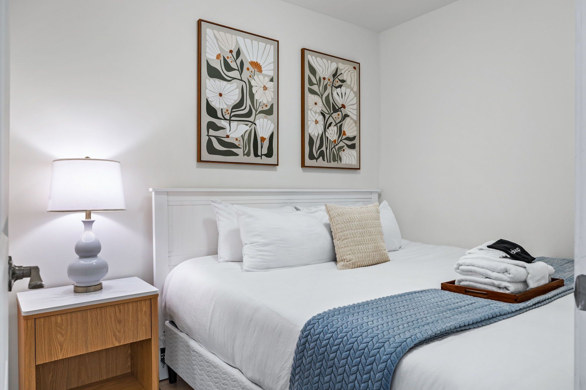 A hotel room with a bed, a nightstand, a lamp, and two wall-mounted artworks.
