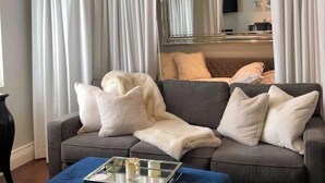 Ein Wohnzimmer mit grauem Sofa, weißen Kissen, einem blauen Hocker und einer Chandelier.