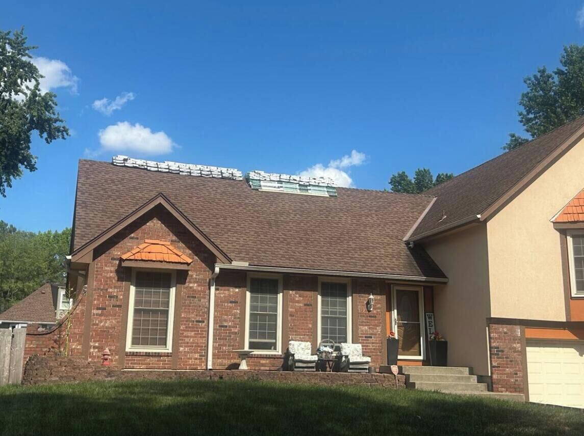 A brick building with a gabled roof, a front porch with two chairs, and a garage.
