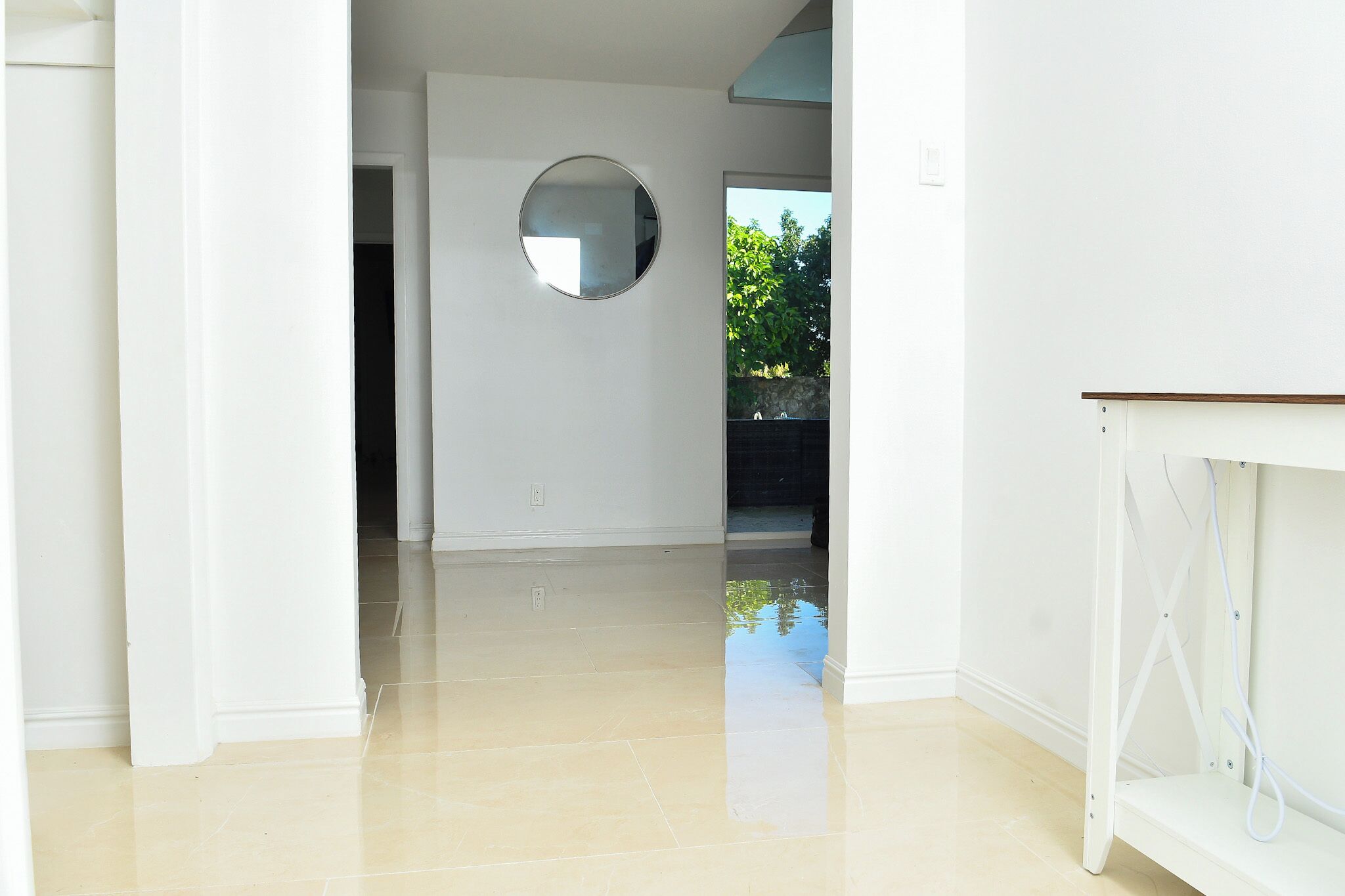 A hallway with a round mirror on the wall, a white door, and a white cabinet with cables.
