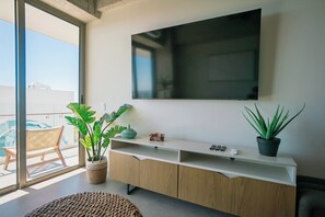 Un salon moderne avec une grande télévision, un meuble en bois, des plantes en pot et une vue sur le balcon.