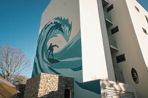 Un bâtiment orné d’une grande fresque représentant un surfeur chevauchant une vague, avec une base en pierre et le chiffre « 3 » sur le côté.