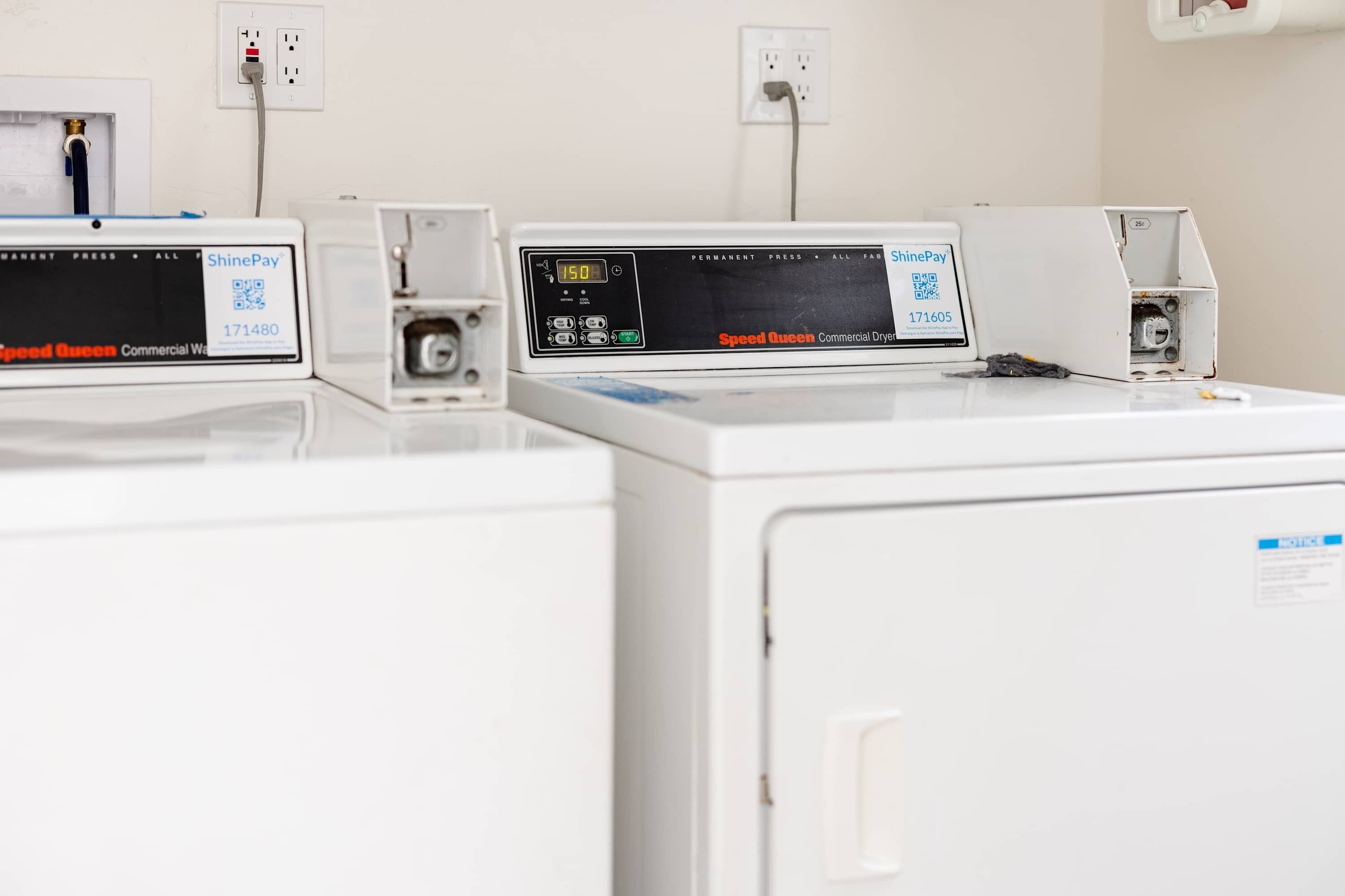 A row of commercial dryers with control panels, each with a QR code and a model number.