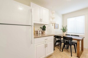 A kitchen with white cabinets, a countertop, a dining table with chairs, and a hanging light fixture. - Beachside Escape in the Heart of OB (San Diego)
