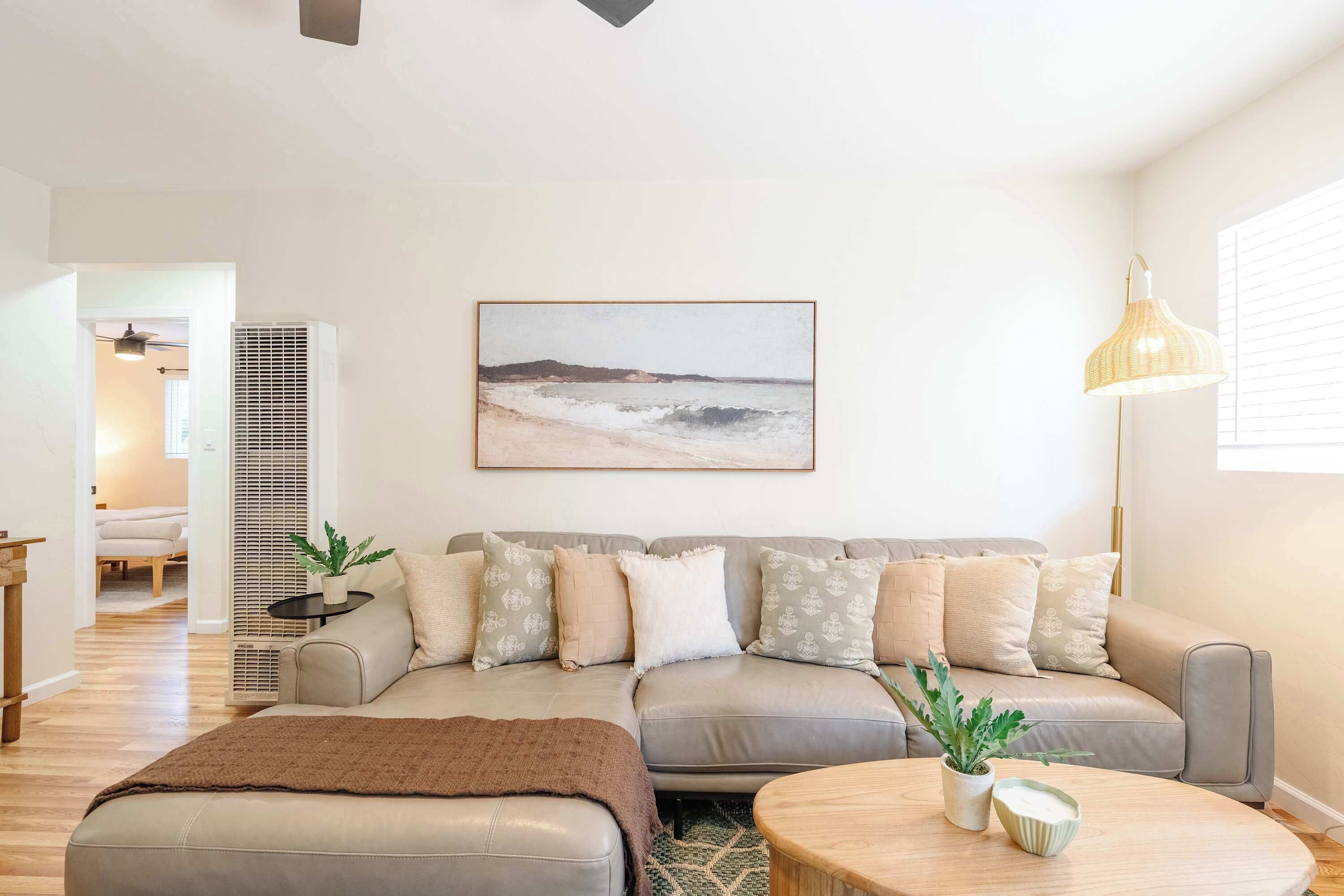 A modern living room with a grey sofa, a coffee table, a painting of a beach, and a floor lamp.