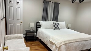 Una camera da letto con un letto, comodini, una sedia, una porta e tende.