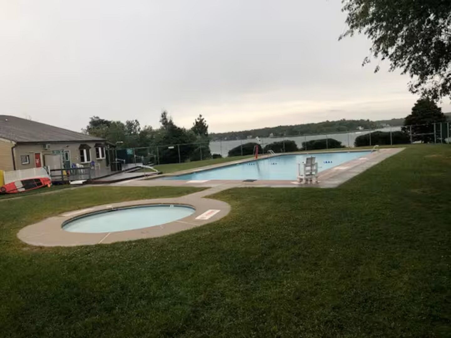 A swimming pool area with a building, a grassy lawn, and a view of a bridge in the background.