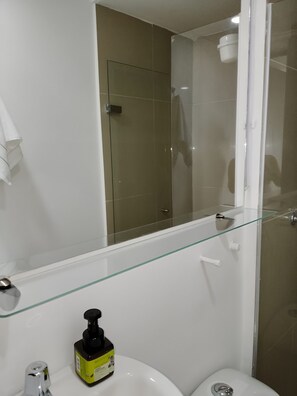 A bathroom with a glass shower enclosure, a white sink with a soap dispenser, and a mirror above the sink. - Beautiful and cozy studio apartment. Refugio Perfecto in Medellín (Medellín)