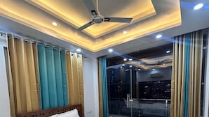 Quarto de hotel moderno com uma cama grande, ventilador de teto e vista para a cidade através da janela.