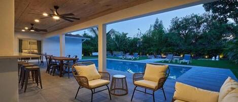 A covered outdoor area with a pool, lounge chairs, and a dining setup.